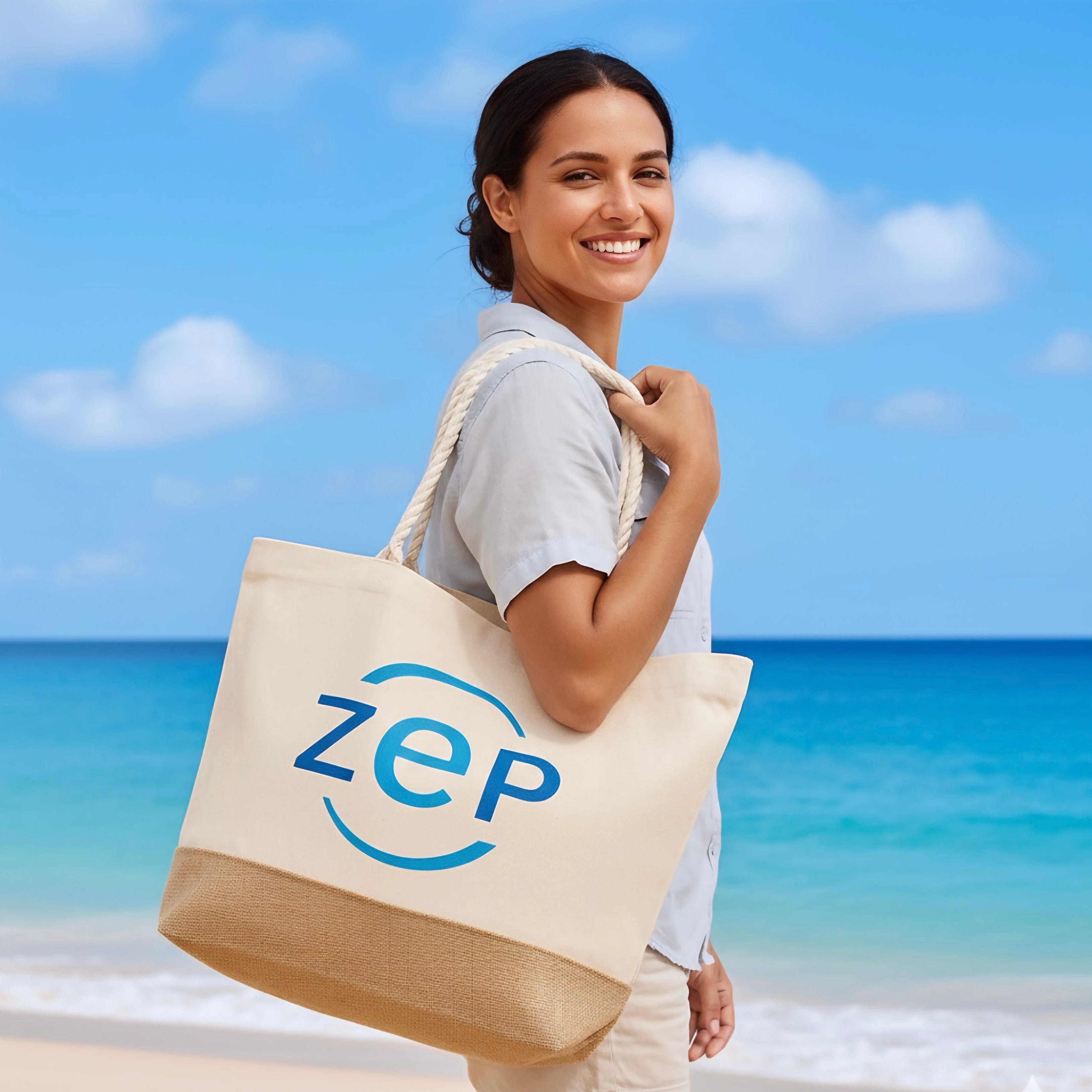 Frau am Strand trägt eine große Stofftasche mit blauem ZEP-Logo über der Schulter und lächelt in die Kamera. Im Hintergrund sind Meer, Strand und blauer Himmel zu sehen.