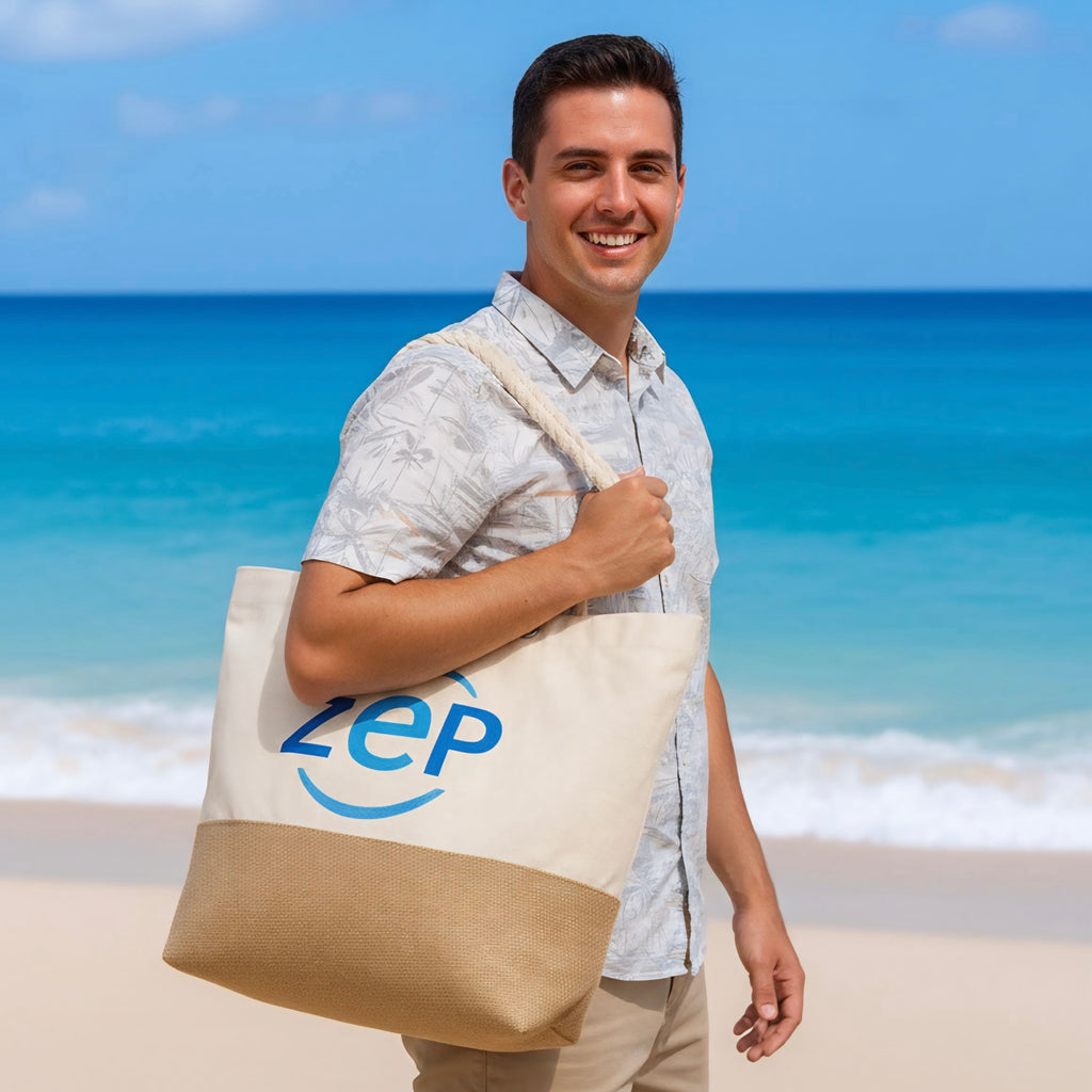 Mann am Strand trägt eine große Stofftasche mit blauem ZEP-Logo über der Schulter und lächelt in die Kamera. Im Hintergrund sind Meer und blauer Himmel zu sehen.