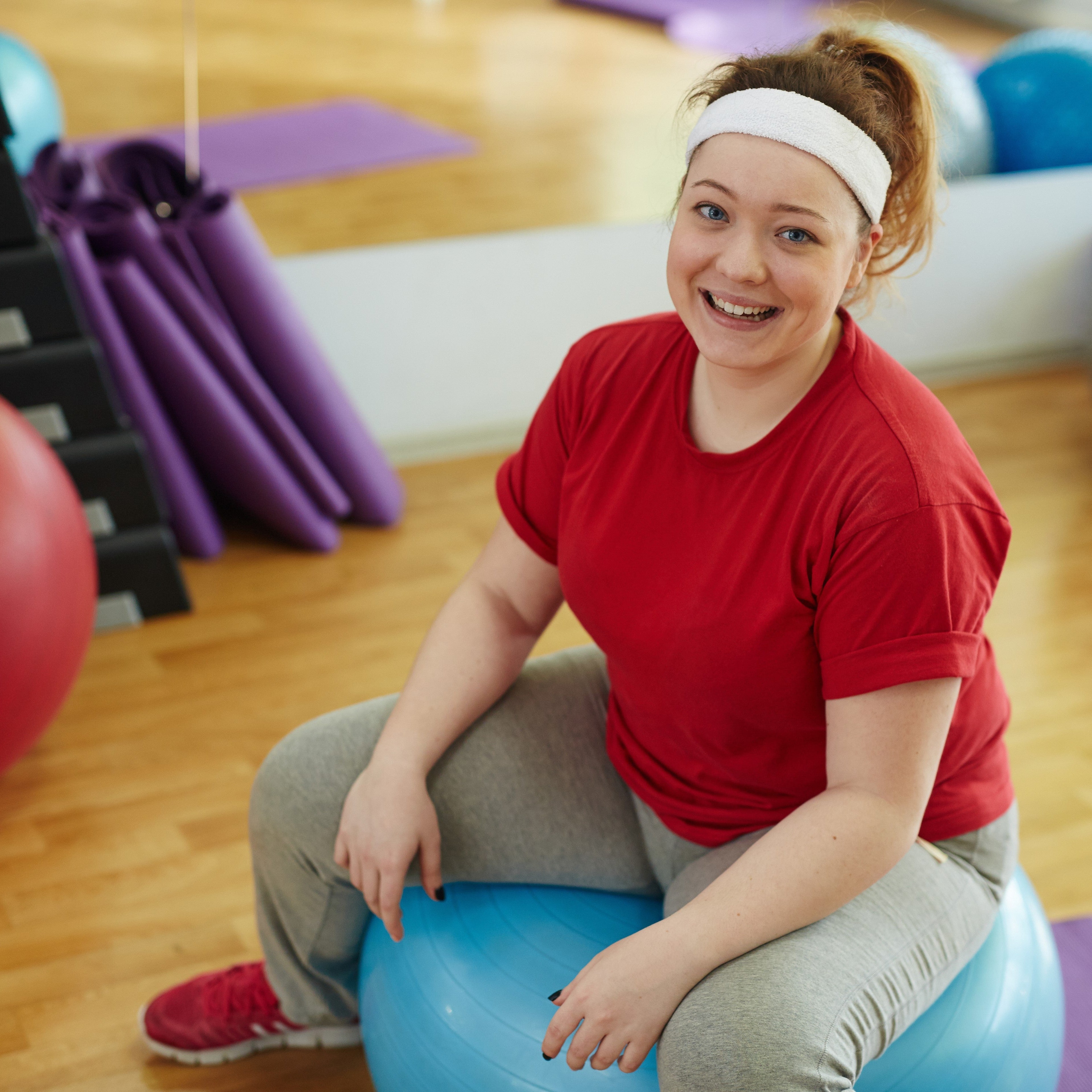 Frau sitzt lächelnd auf einem Gymnastikball im Rahmen eines Gesundheits- oder Bewegungsprogramms